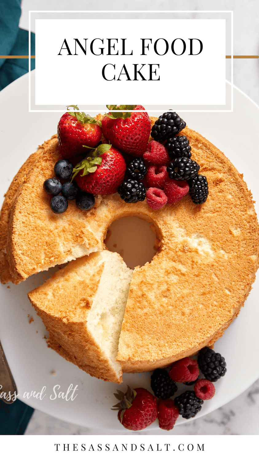 A delicious-looking angel food cake is topped with an assortment of fresh berries, including strawberries, blackberries, blueberries, and raspberries. A slice has been cut out, revealing the light and airy interior of the cake. "Angel Food Cake" is written above the cake.