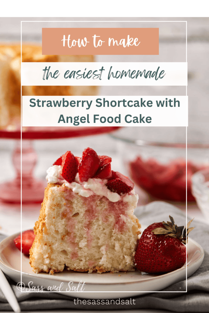 A slice of strawberry shortcake made with angel food cake on a white plate, topped with whipped cream and fresh strawberries. A whole strawberry and a fork are next to the slice. In the background, there's another slice on a red plate.