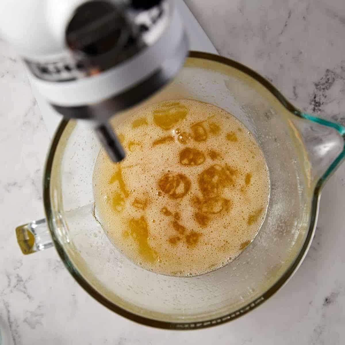 A glass mixing bowl with frothy liquid and sits under a stand mixer on a marble countertop, ready for the next step in delicious angel food cake recipes.