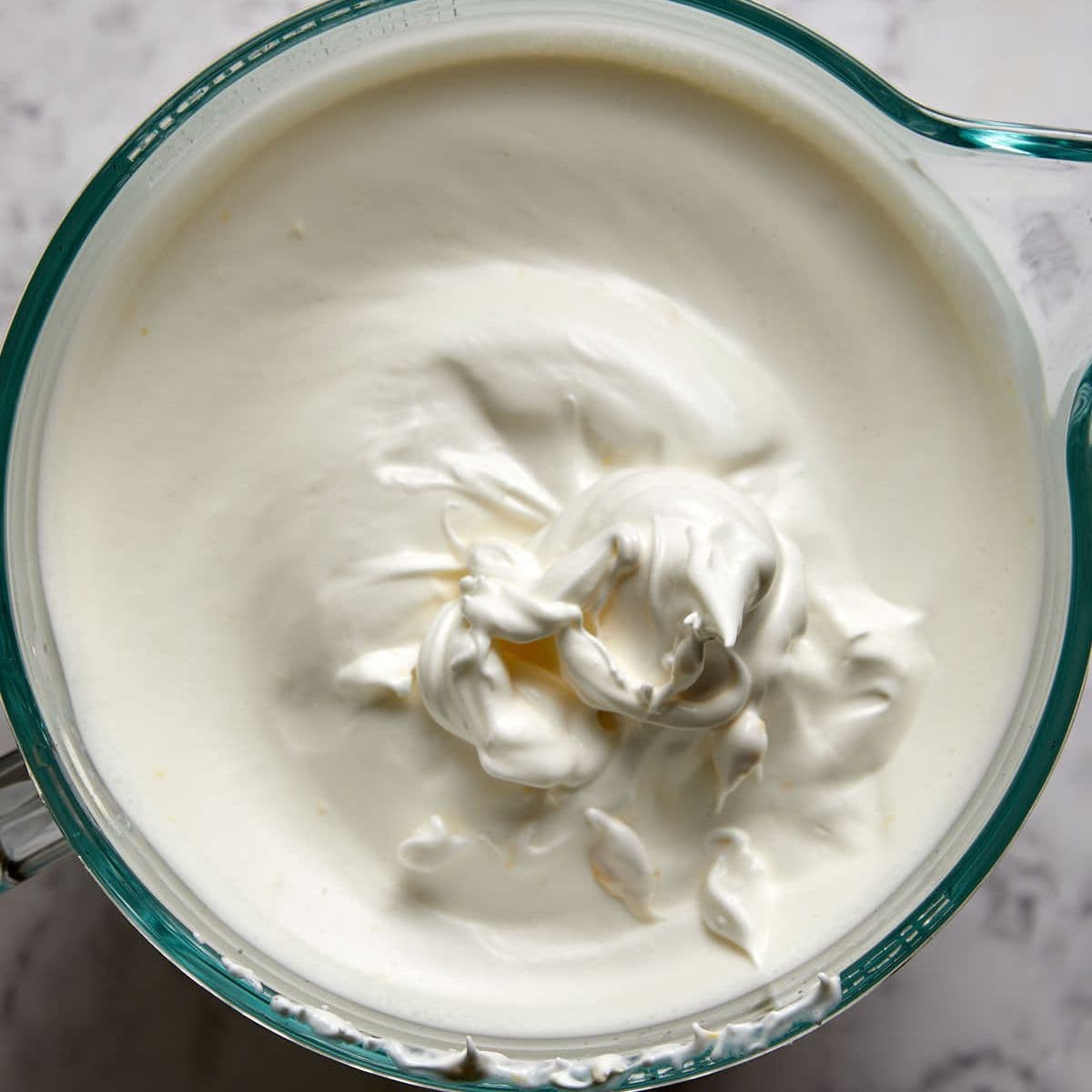 A glass bowl filled with thick, freshly egg whites, showing soft peaks on the smooth surface—perfect for topping your favorite angel food cake.