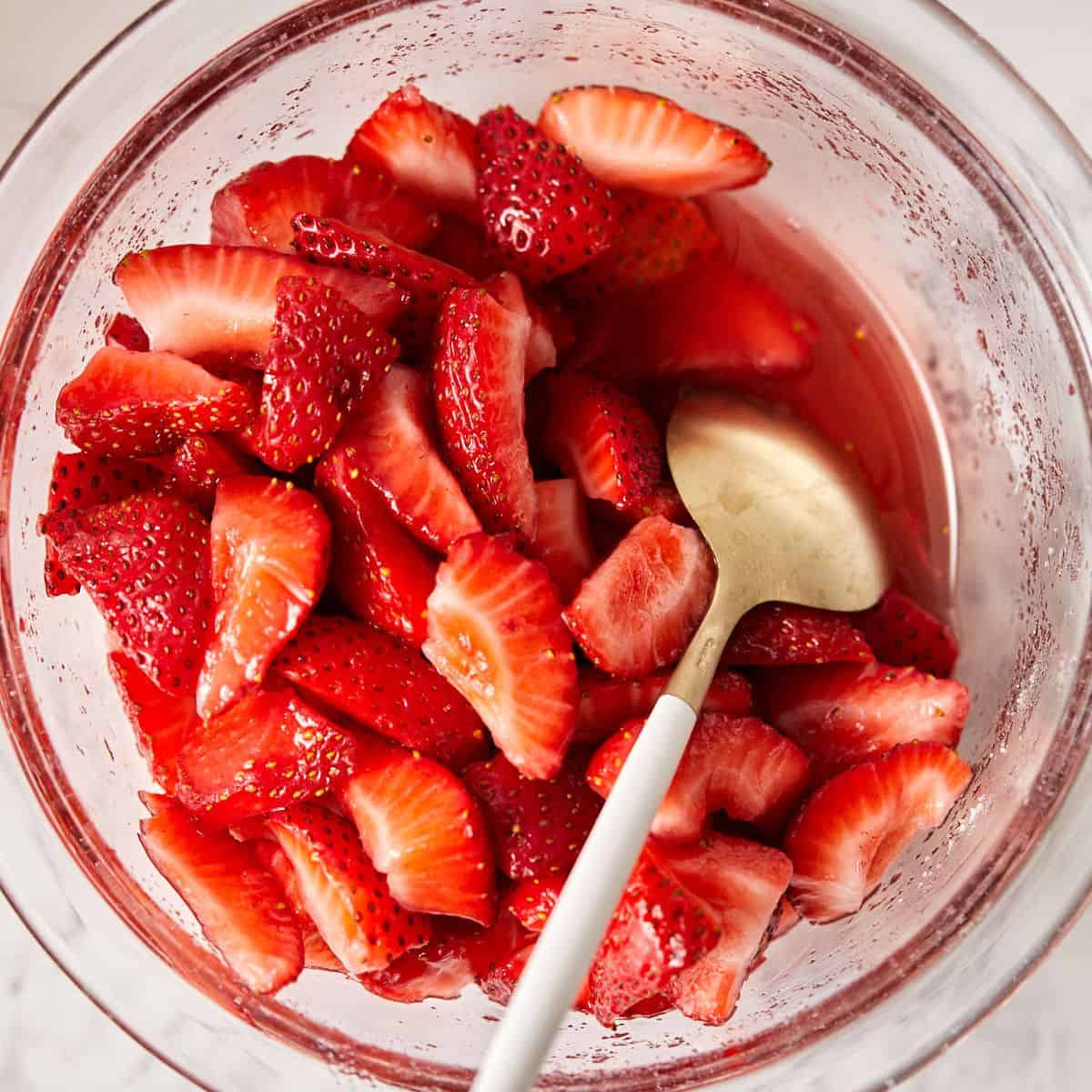 Overhead view of macerated strawberries in a bowl with a spoon.