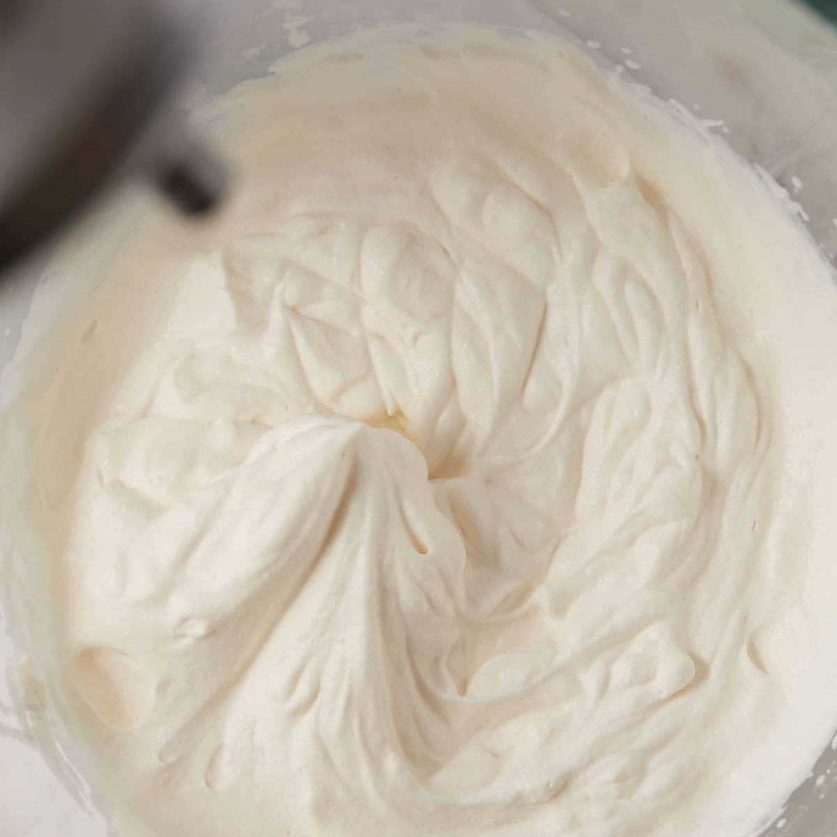 Overhead view of whipped cream in the bowl of a stand mixer.