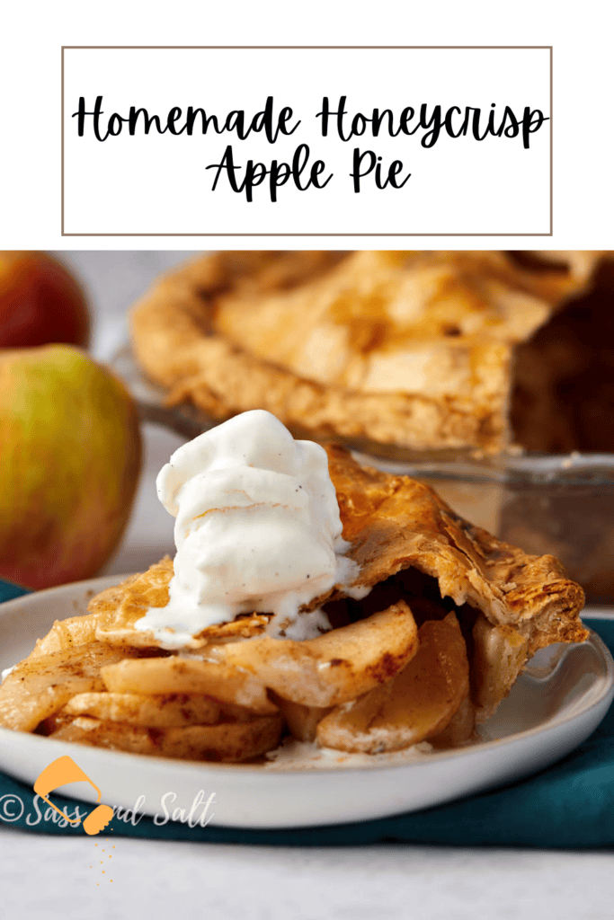 A slice of homemade Honeycrisp apple pie topped with a scoop of vanilla ice cream on a plate. The whole pie and an apple are blurred in the background. Text at the top reads "Homemade Honeycrisp Apple Pie.