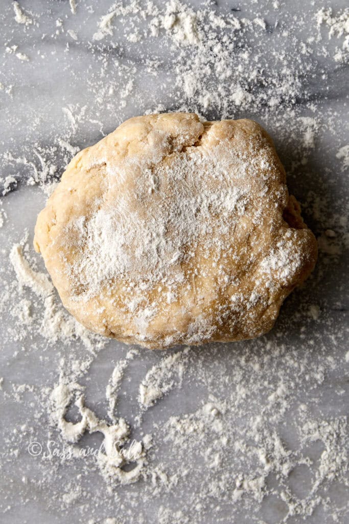 A ball of raw dough sprinkled with flour rests on a lightly floured marble surface.