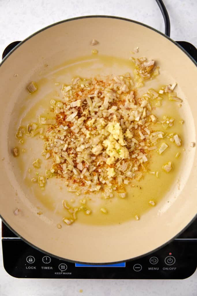 Chopped garlic and onions sautéing in olive oil in a beige pan on an electric stove.