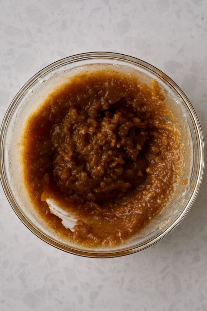 A glass bowl filled with a thick, brown paste-like mixture sits on a light-colored countertop. The texture appears smooth with a slightly coarse surface.