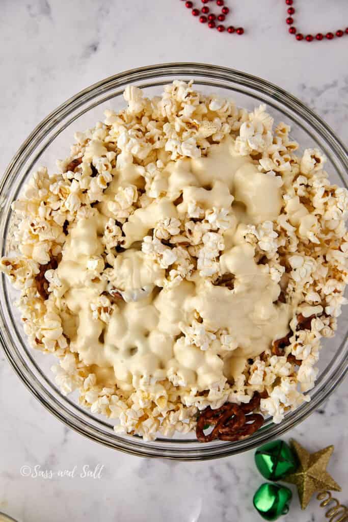 A bowl of popcorn mixed with chocolate, placed on a marble surface. Red beads and gold and green star-shaped decorations are scattered nearby.