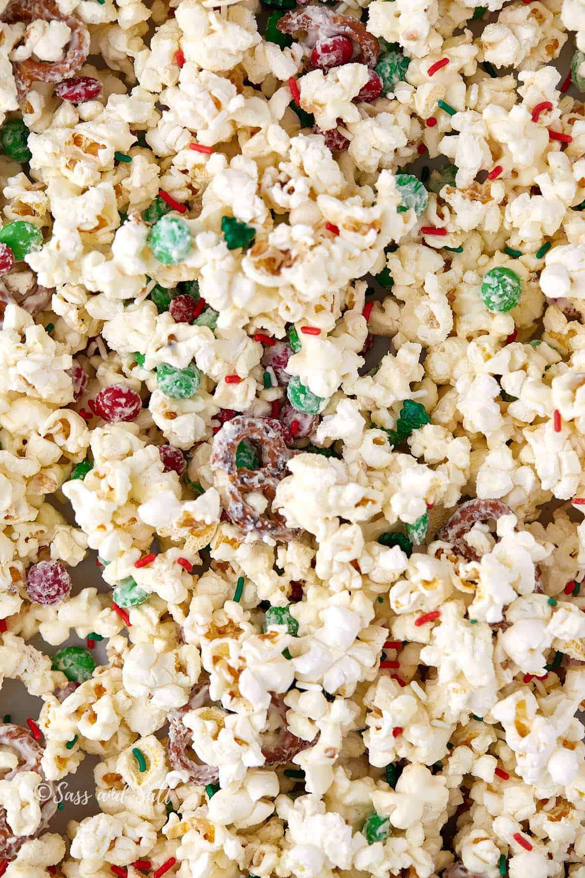 A close-up of festive popcorn mixed with green and red candies and multicolored sprinkles. The popcorn is lightly coated, giving a sweet and colorful appearance suitable for holiday celebrations.