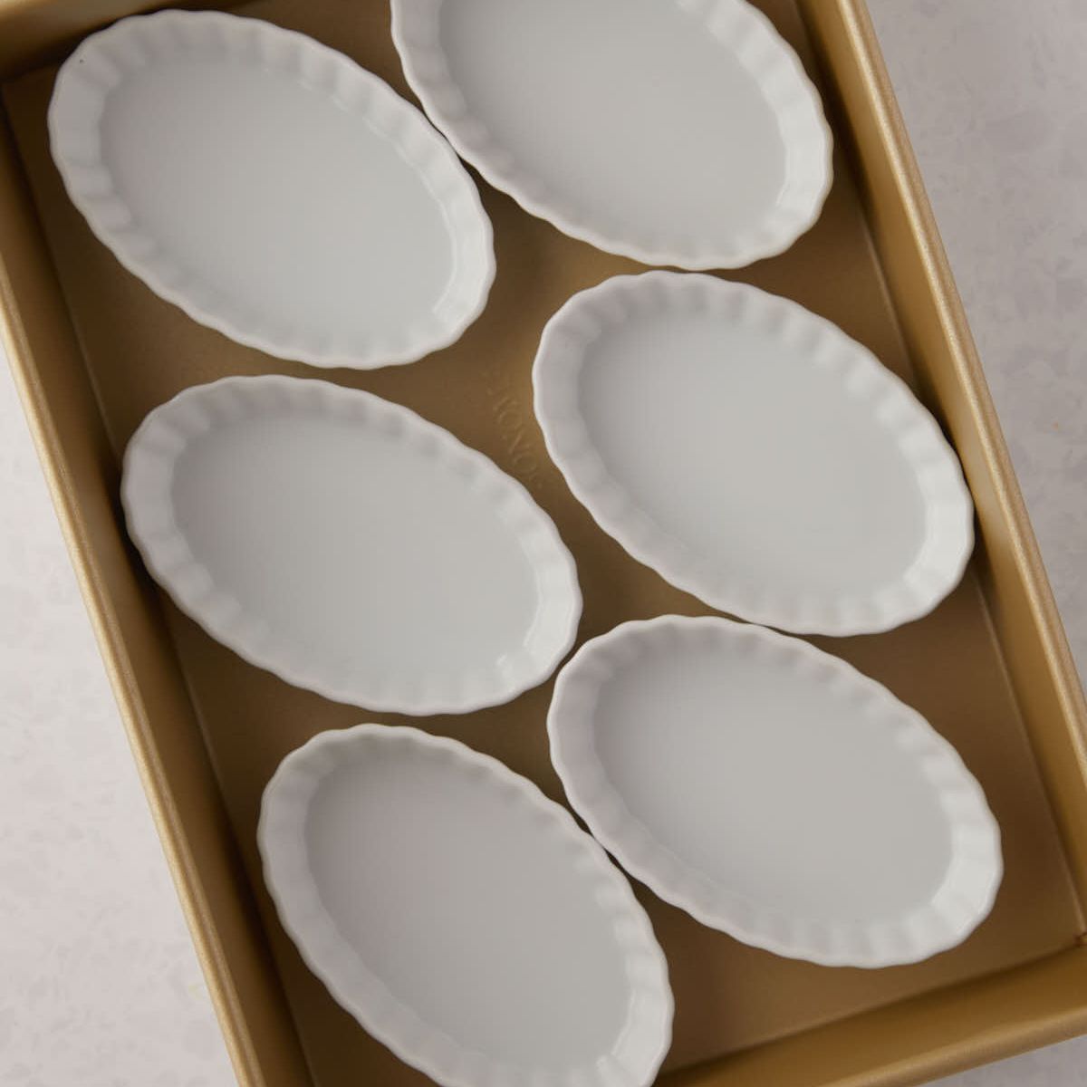 Empty oval ramekins in a baking pan.