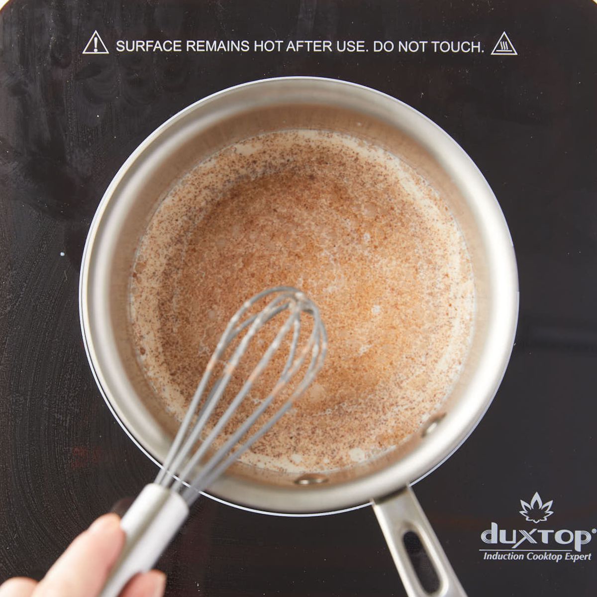 Warm cream and spices whisked in a saucepan.