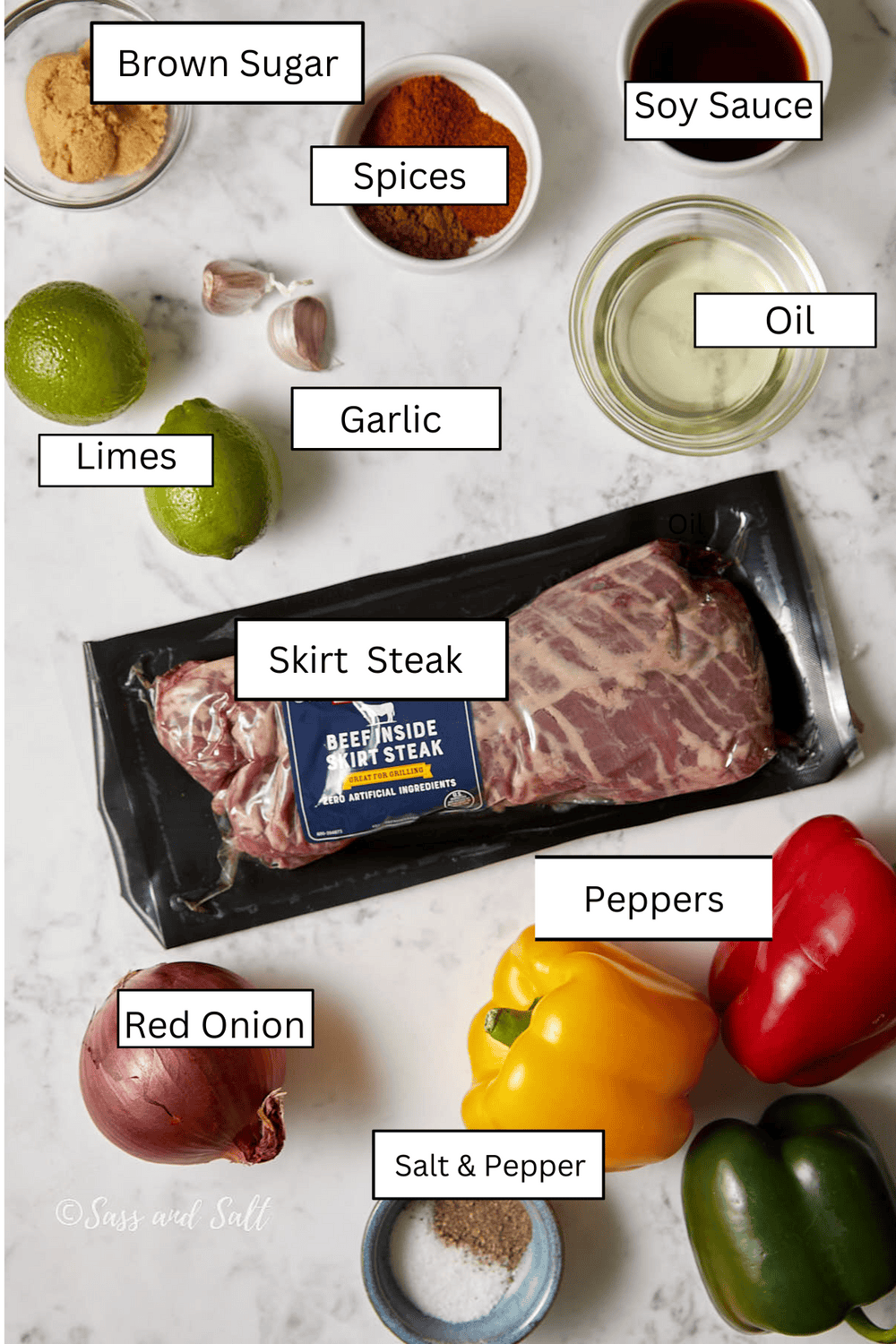 Top view of ingredients for a skirt steak dish on a white surface. Items include brown sugar, spices, soy sauce, oil, limes, garlic, a package of skirt steak, red onion, salt and pepper, and colorful bell peppers.