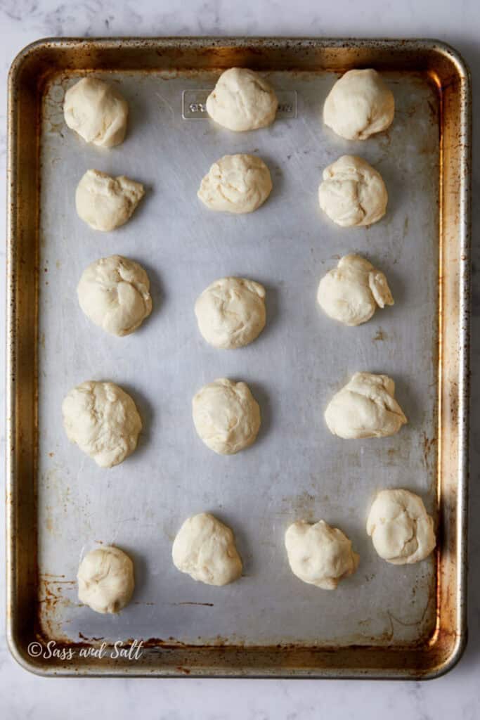 Eighteen unbaked dough balls spaced evenly on a large, worn baking sheet.