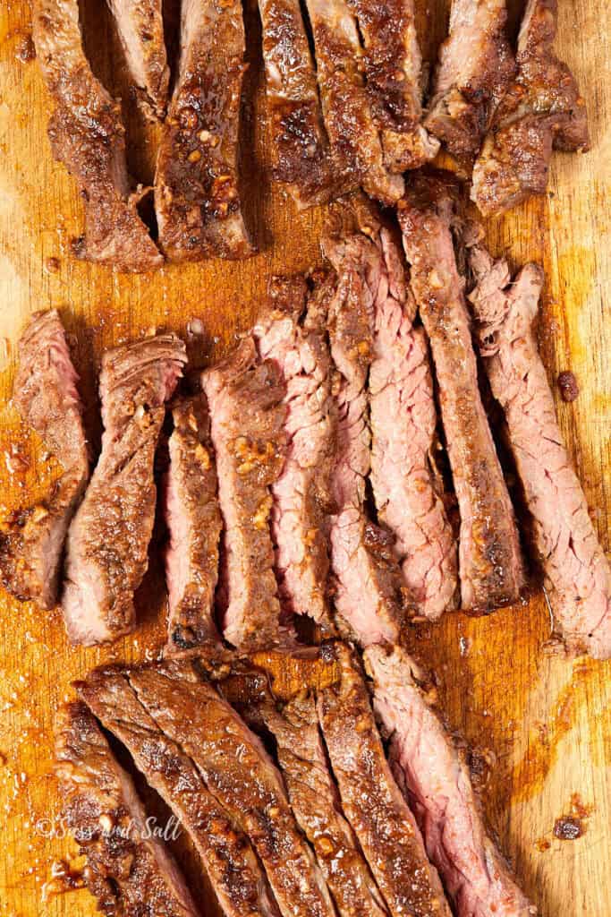 Sliced grilled steak on a wooden cutting board, showcasing juicy pieces with a well-browned exterior and a pink, tender interior.