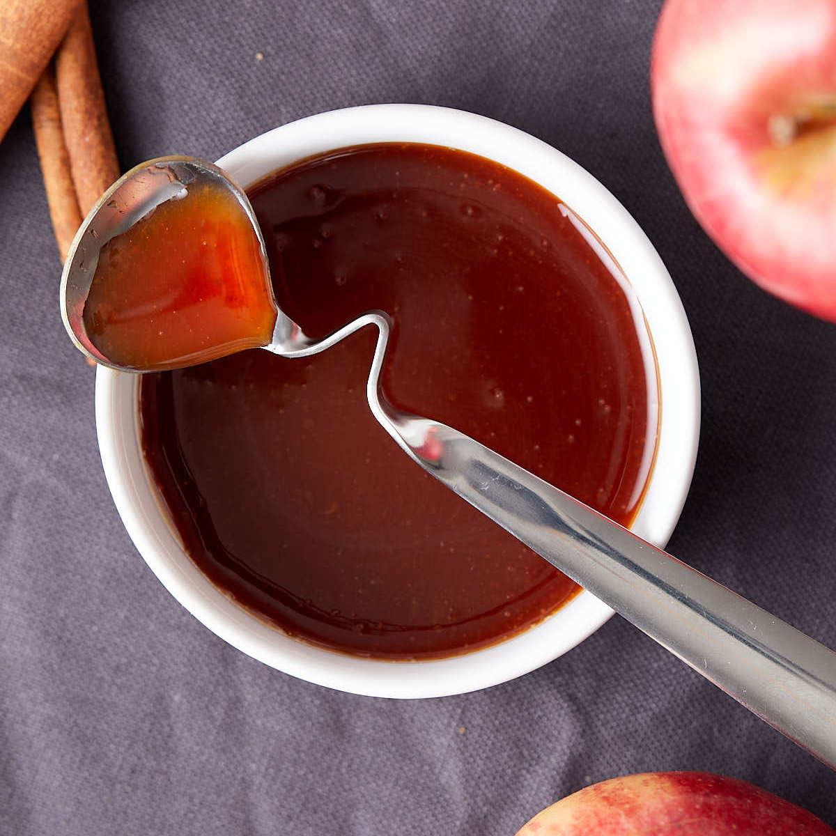 Apple cider syrup on a spoon sitting on a white bowl.