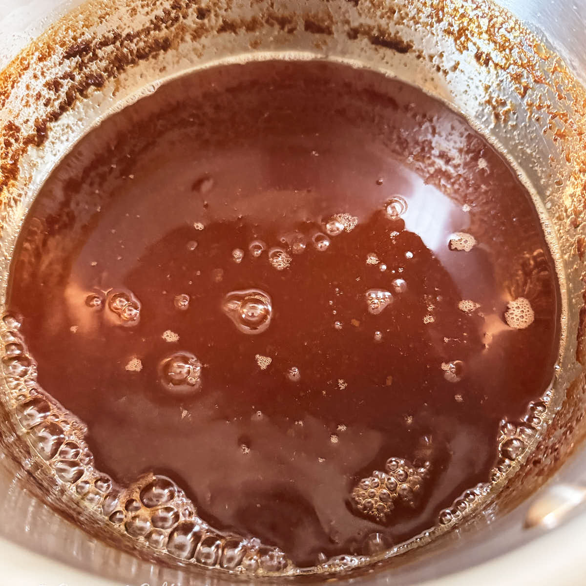 Dark copper bubbles covering the surface of boiled cider.