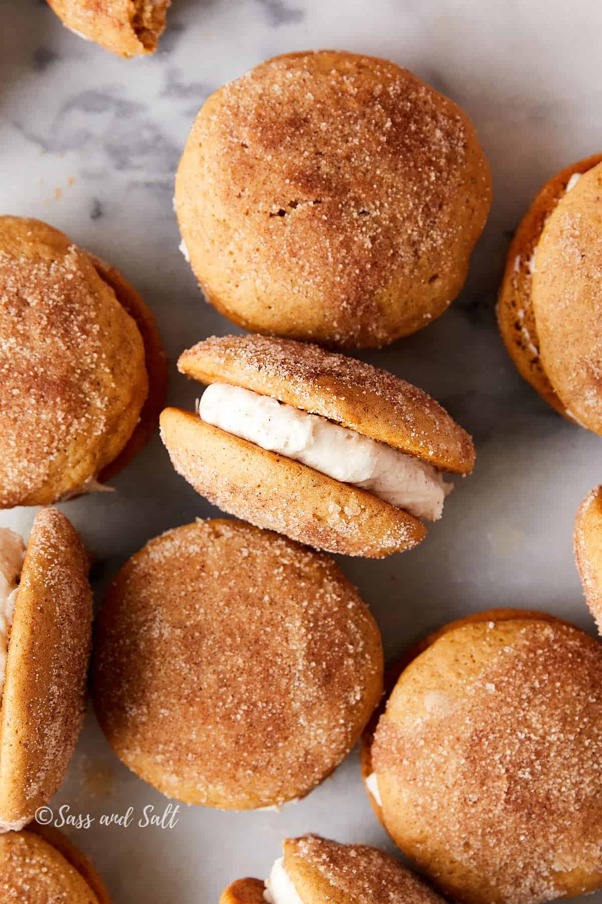 Apple cider whoopie pies on marble with one turned to show the cream cheese filling.