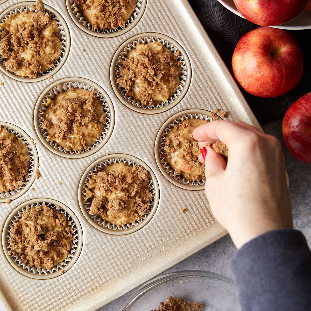 Sprinkling cinnamon streusel on muffin batter.