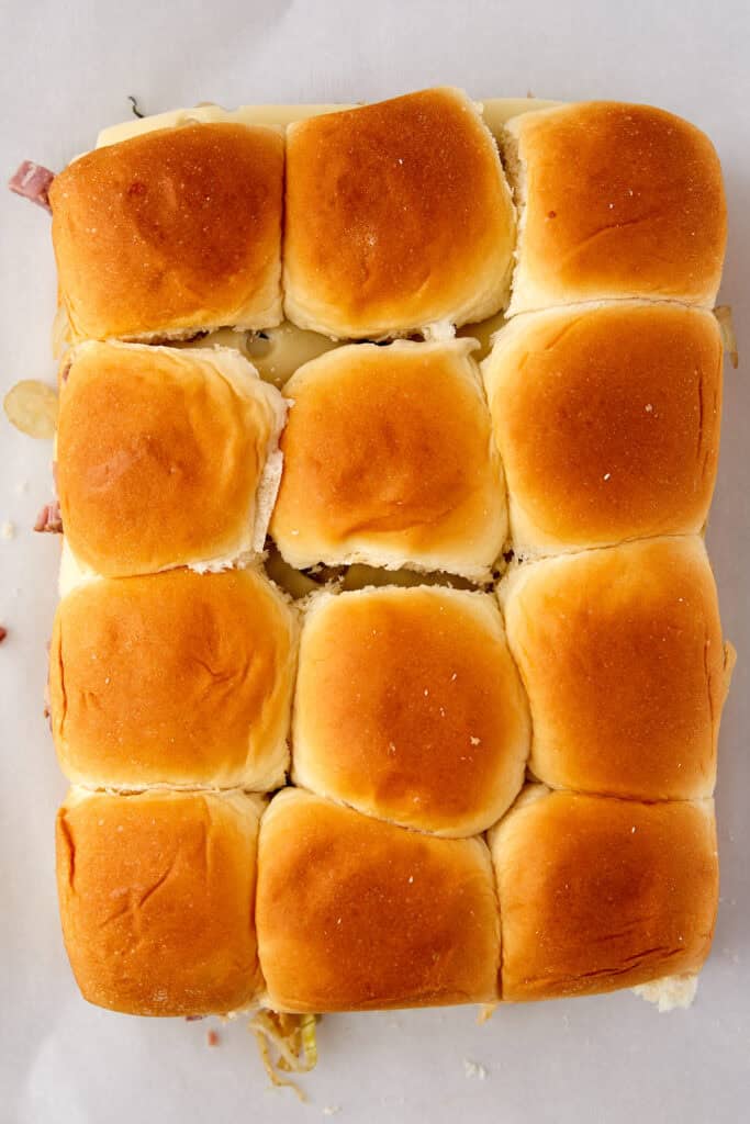 Twelve golden-brown slider buns arranged in a rectangular grid on a white surface, viewed from above.