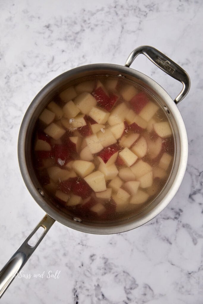 A saucepan filled with diced red potatoes simmering in water, placed on a white marble countertop.