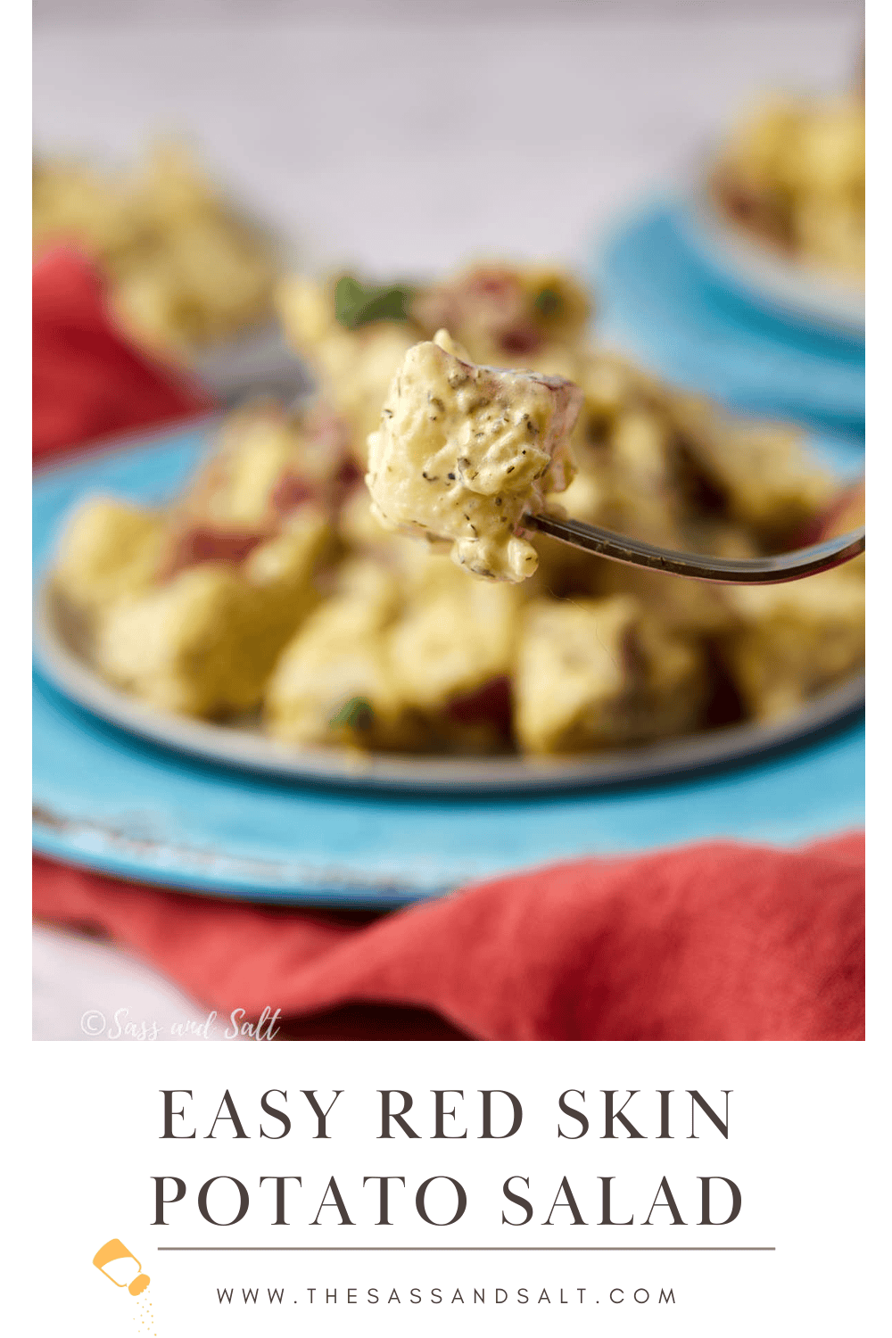 A fork holding a bite of creamy red skin potato salad hovers above a plate of the same salad. The text below reads, "Easy Red Skin Potato Salad" with a website link www.thesassandsalt.com.