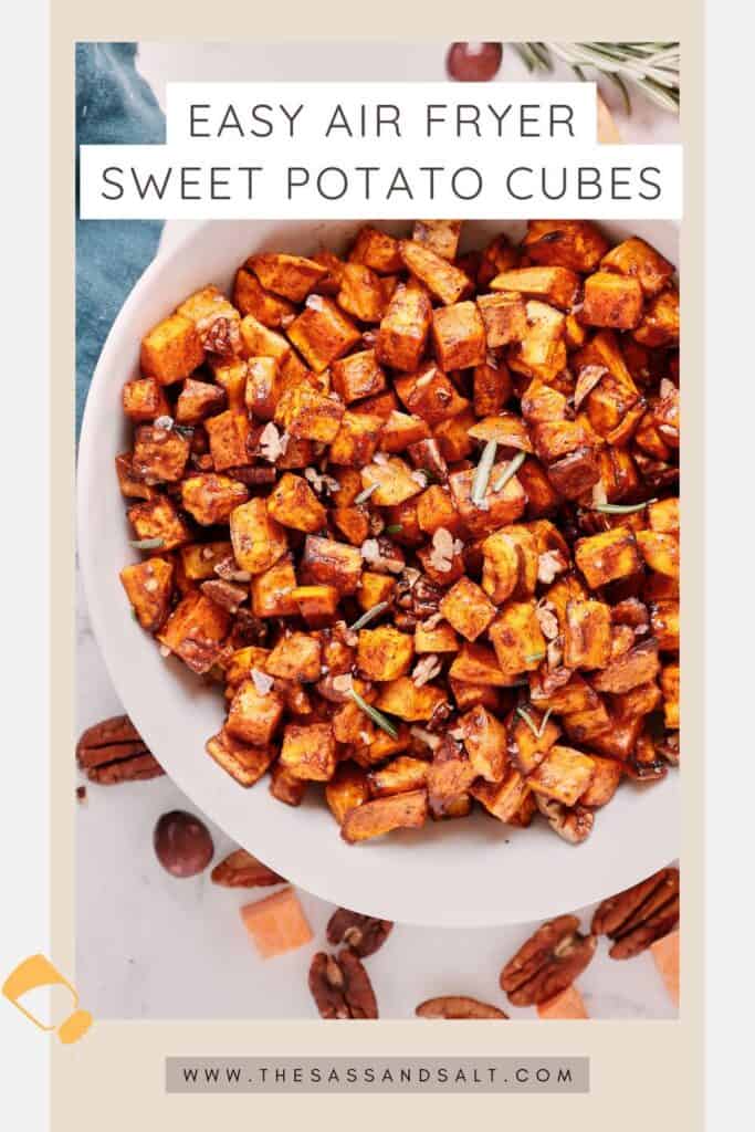 A bowl filled with seasoned, air-fried sweet potato cubes, garnished with herbs. Pecans, rosemary, and sweet potato pieces are scattered around. Text above the bowl reads "Easy Air Fryer Sweet Potato Cubes.”.