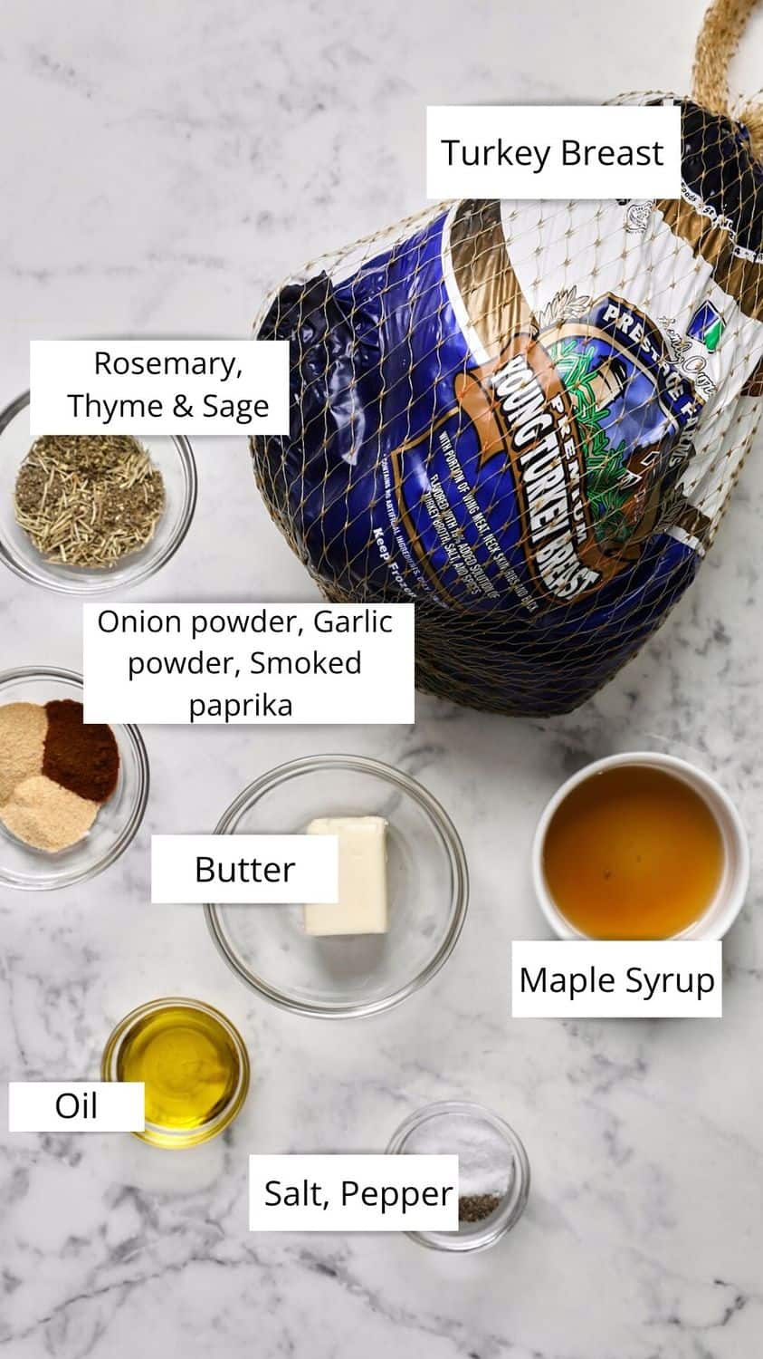 Overhead view of Turkey Breast in packaging, surrounded by small bowls of dried herbs, spices, butter, oil, maple syrup, salt, and pepper all labeled on a white marble surface.