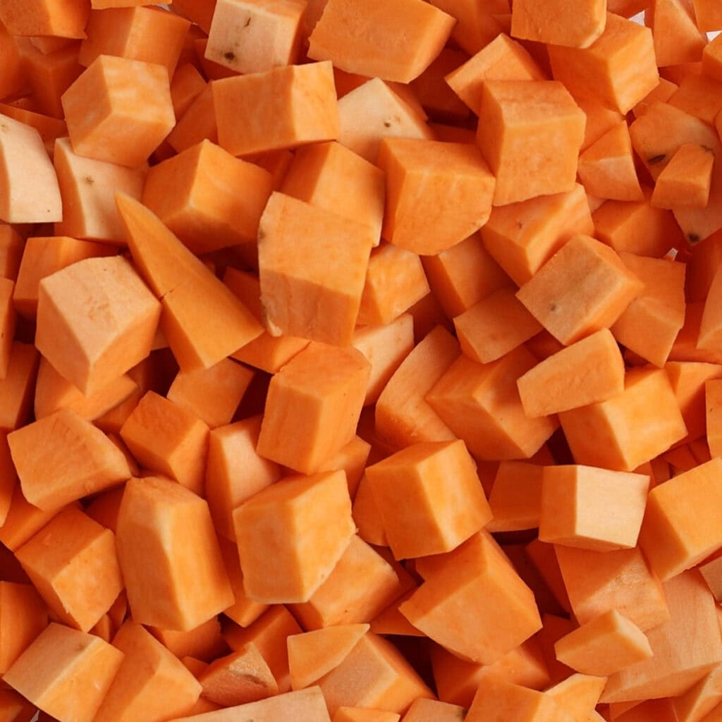 A close-up view of many small, uniformly chopped orange sweet potato cubes piled together.