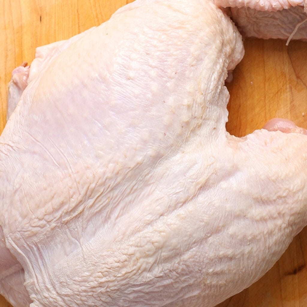 A close-up of a raw, uncooked turkey breast with skin on, resting on a wooden cutting board—perfect for preparing dishes like air fryer turkey breast.