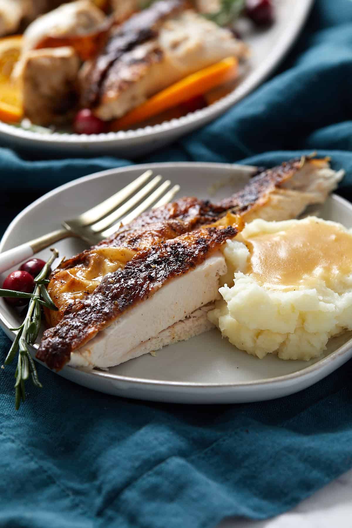 A plate with a slice of air fryer turkey breast garnished with rosemary and cranberry, served alongside a scoop of mashed potatoes topped with gravy. A fork rests on the plate.