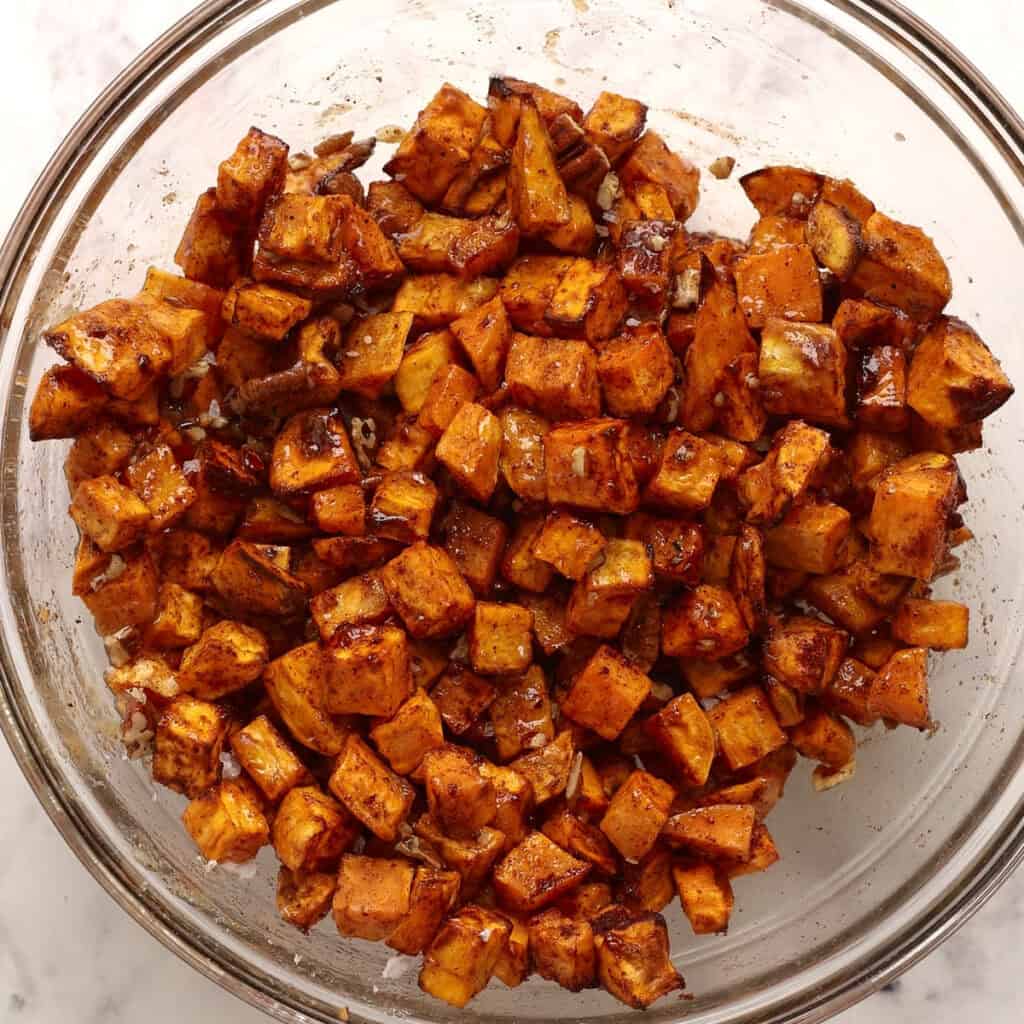 A glass bowl filled with roasted sweet potato cubes seasoned with spices, showing a golden-brown, slightly caramelized appearance.
