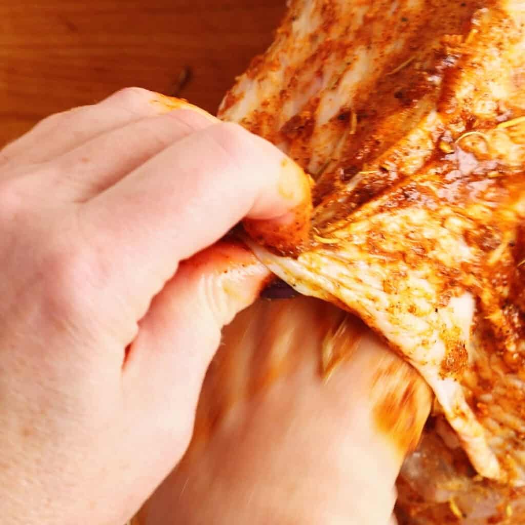 A close-up of hands rubbing orange-brown seasoning under the skin of raw boneless turkey breast, preparing it on a wooden surface—perfect for making juicy air fryer turkey breast.