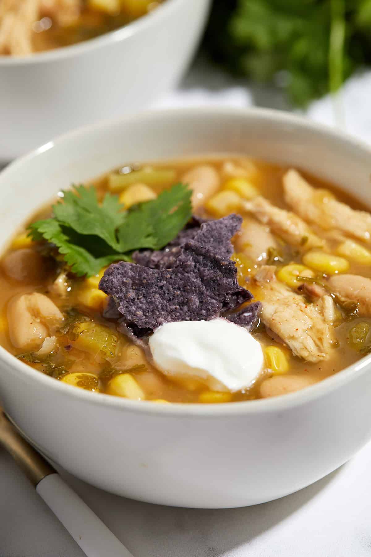 A bowl of leftover turkey verde tortilla soup topped with a dollop of sour cream, blue corn tortilla chips, and a sprig of cilantro, with visible corn, white beans, and shredded turkey.
