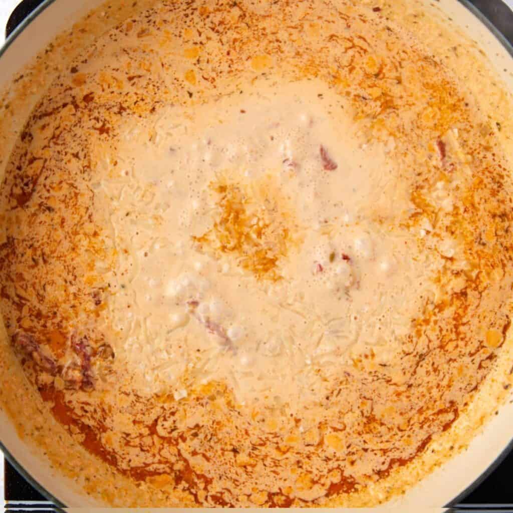 A close-up of a creamy, sauce with visible oil separation and small chunks of ingredients in a pot.