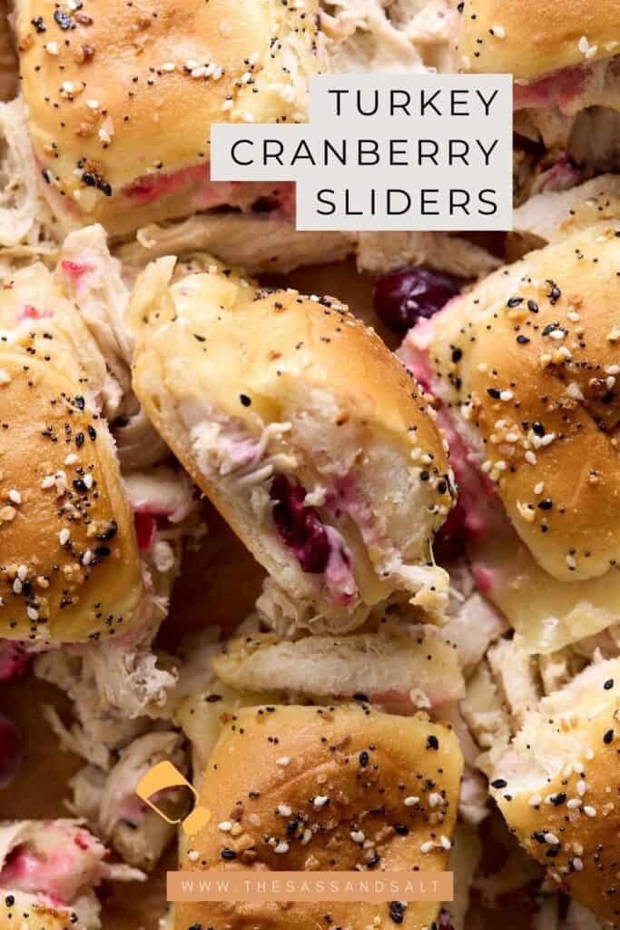 Close-up of turkey cranberry sliders on everything buns, filled with shredded turkey and cranberry sauce. The text “Turkey Cranberry Sliders” is overlaid, and a website link appears at the bottom.