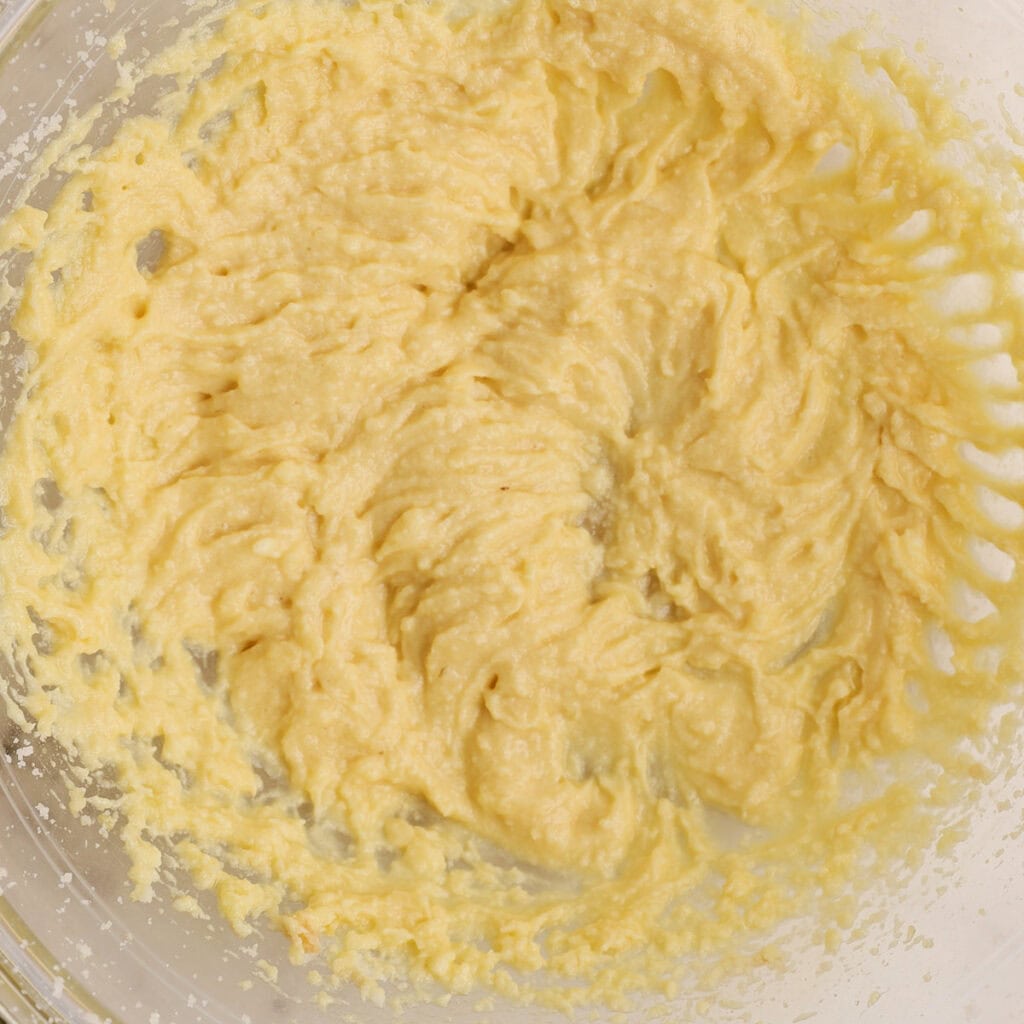 A close-up of a glass mixing bowl filled with creamy, yellow cake batter, showing a smooth and slightly textured consistency.