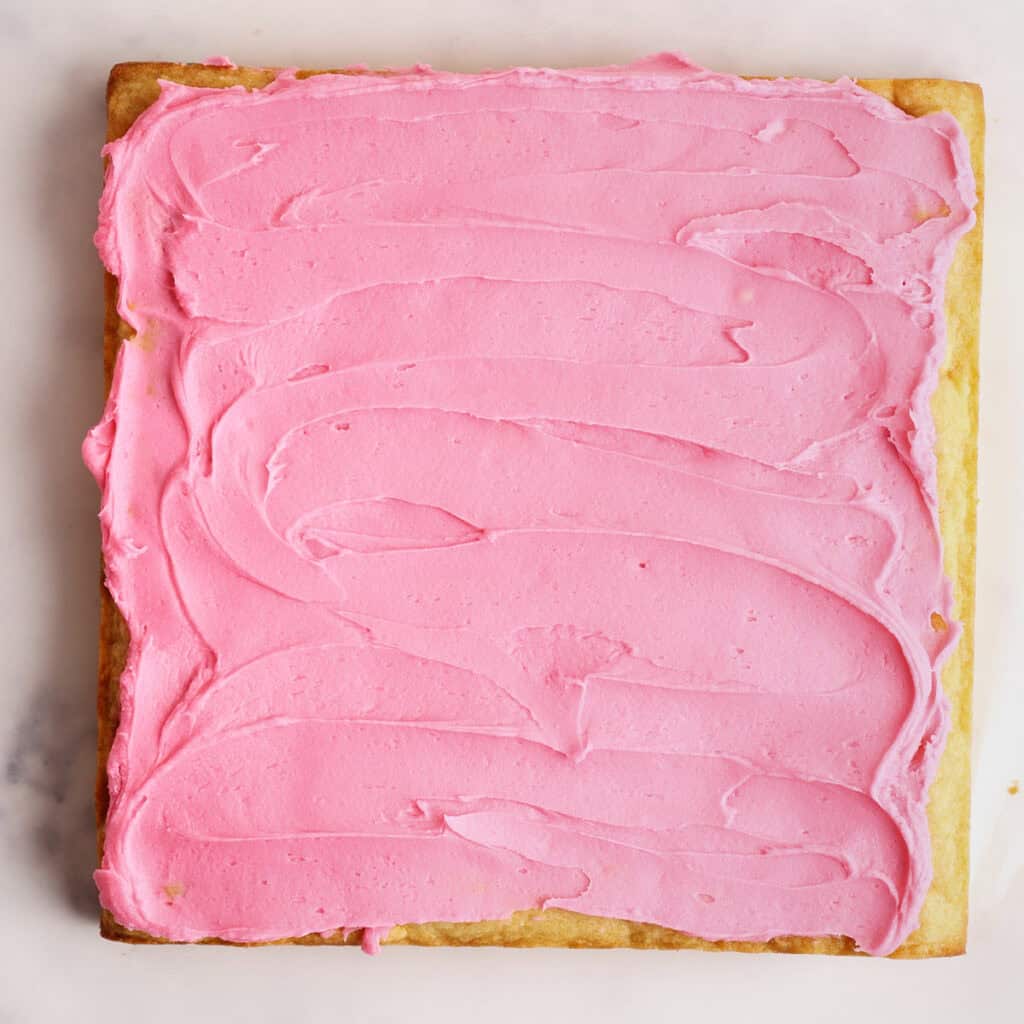 A rectangular sugar cookie with smooth, bright pink frosting spread evenly on top, photographed on a light marble surface.