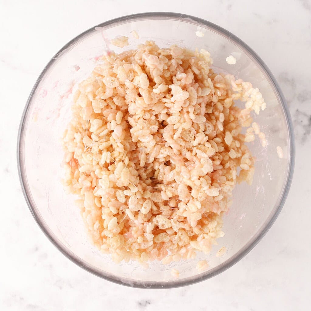A glass bowl filled with Rice Krispies cereal mixed with melted marshmallows, viewed from above on a white marble surface.