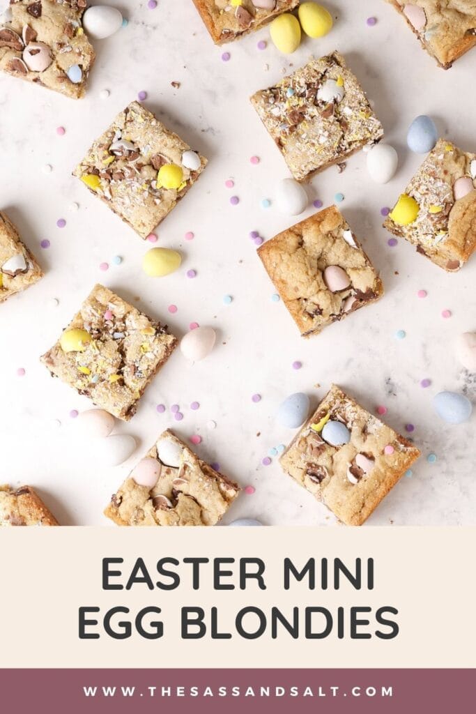 Top view of square blondie bars with mini candy eggs on a white surface, scattered with extra candy eggs and sprinkles. Text at the bottom reads "Easter Mini Egg Blondies" and includes a website link.