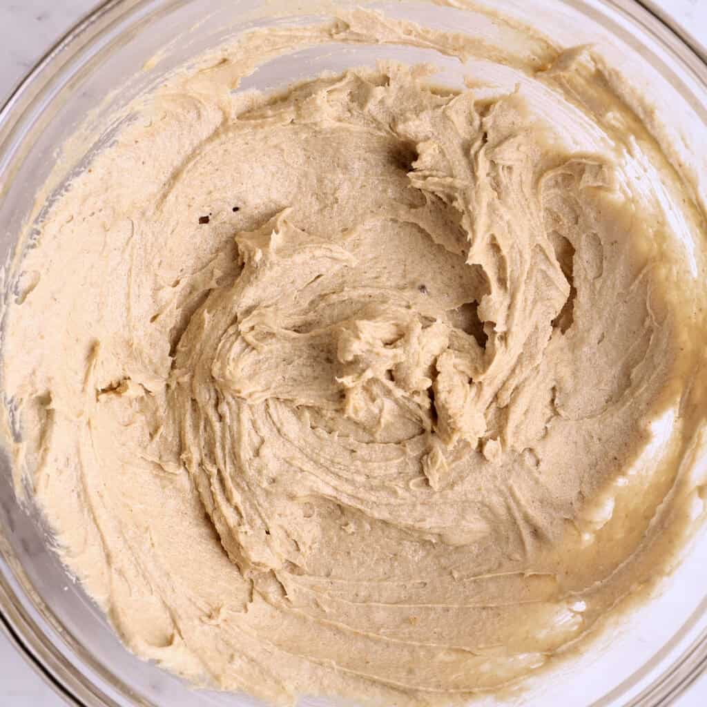 A glass bowl filled with creamy, light brown cookie dough, swirled and smoothed, ready for baking.