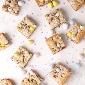 Top view of cookie bars with crushed chocolate eggs and mini candy eggs scattered on a white marble surface, along with small pastel confetti candies.