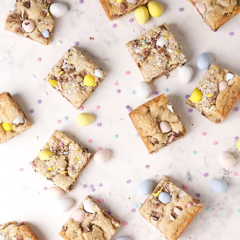 Top view of cookie bars with crushed chocolate eggs and mini candy eggs scattered on a white marble surface, along with small pastel confetti candies.