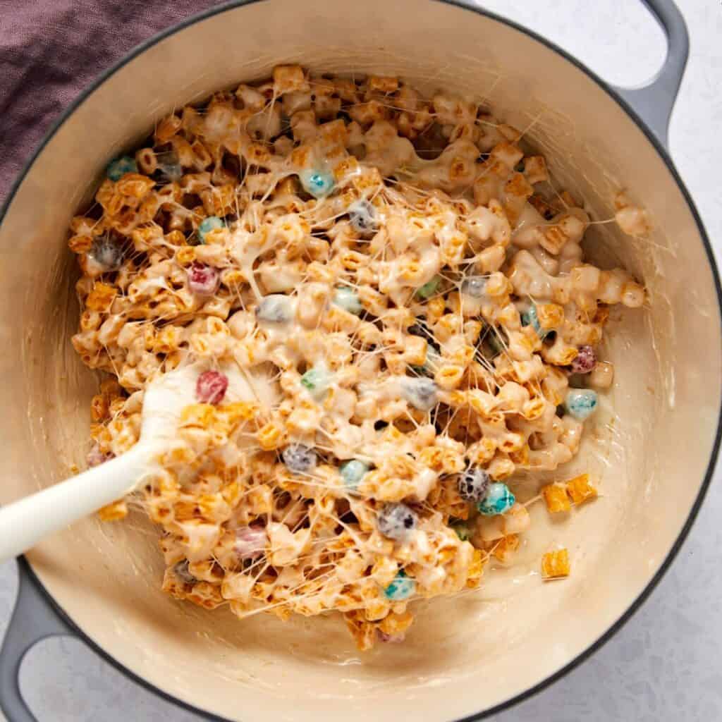 Captain Crunch cereal being folded into melted marshmallow mixture.
