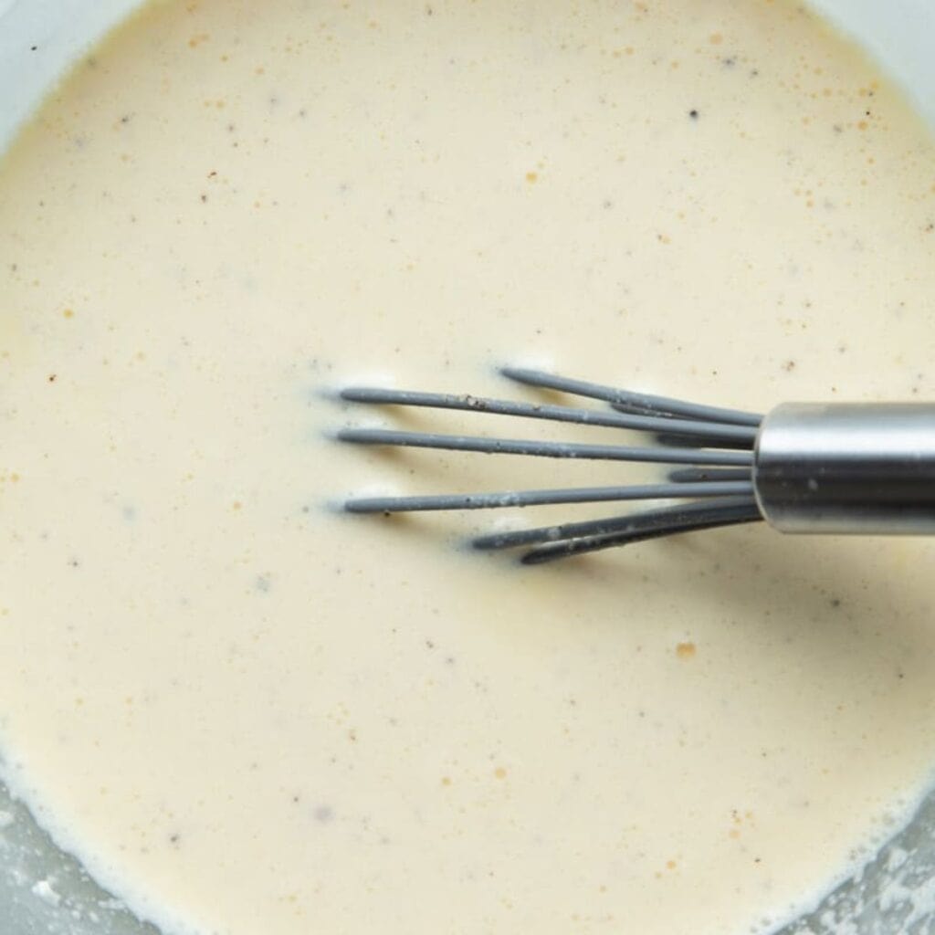 Whisking eggs, cream, milk, cornstarch, and warm spices together for a crustless ham and leek quiche custard.
