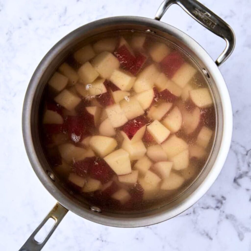 A pot filled with chopped red potatoes simmering in water, seen from above on a white marble surface.