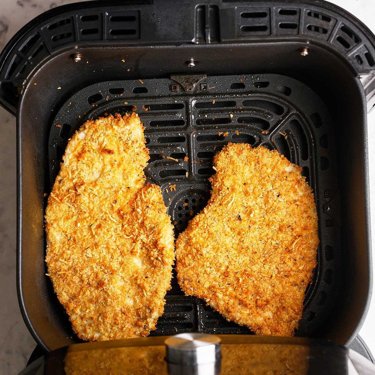 Two crispy breaded thin sliced chicken breast cutlets cooking in a black air fryer basket, golden brown after 4 to 5 minutes at 400°F.