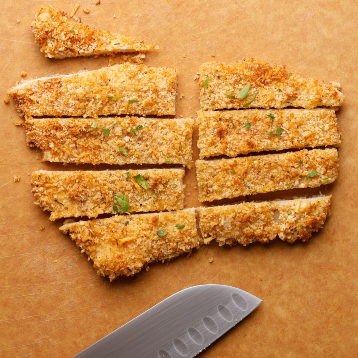 Crispy air fryer chicken cutlet sliced into half-inch strips on a wooden cutting board, ready to layer into a wrap.