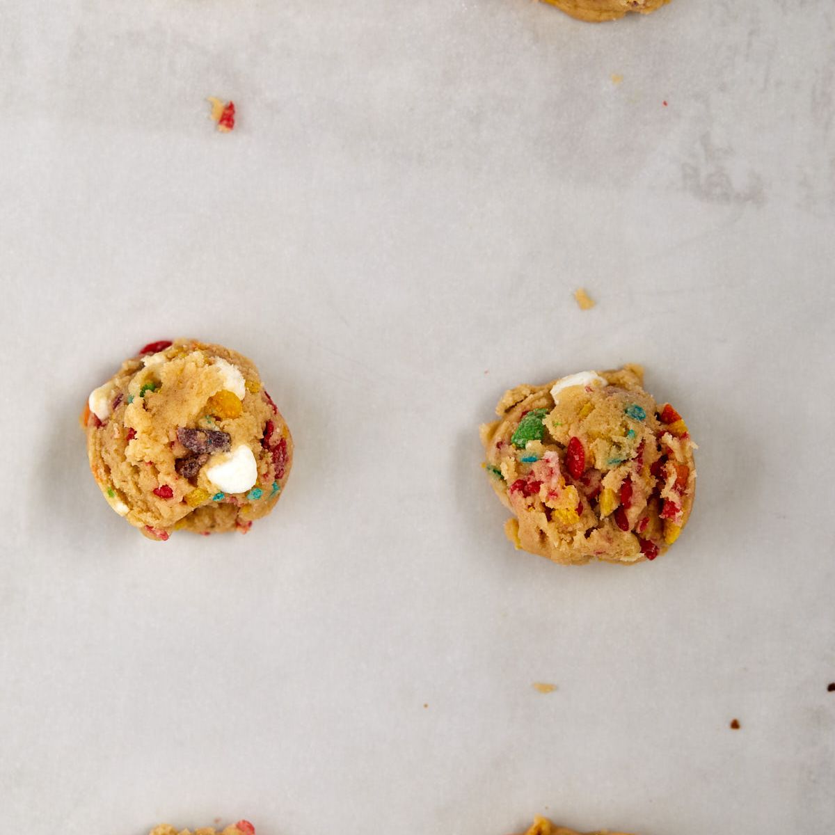 Fruity Pebbles cookie dough balls with cereal and marshmallows on a parchment-lined sheet.