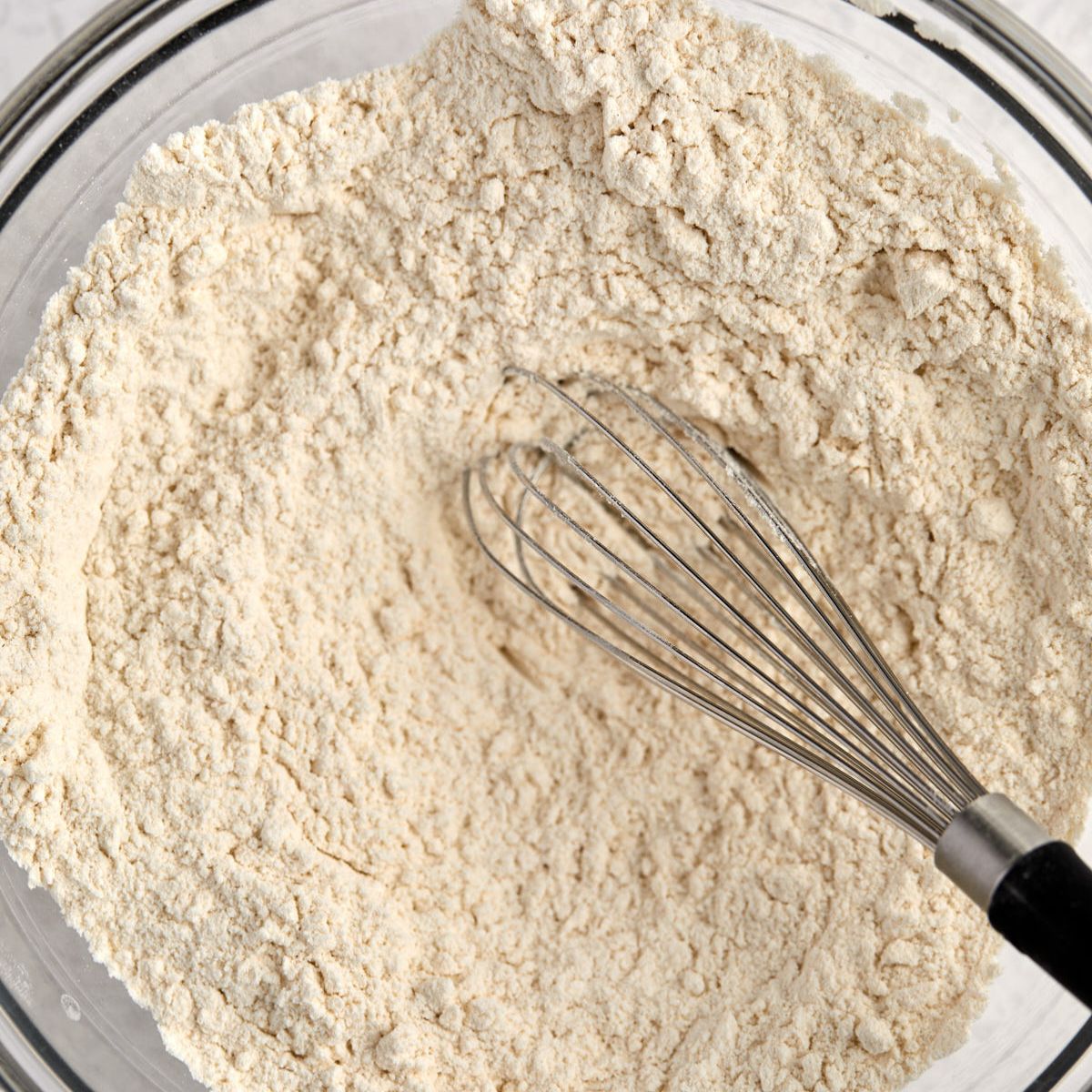 Flour, baking powder, and baking soda whisked together in a glass bowl.