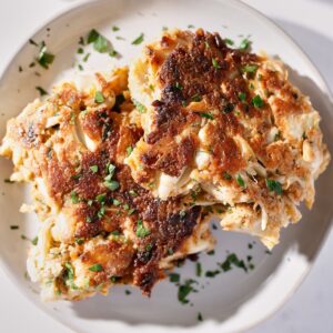 Two golden-brown crab cakes garnished with chopped parsley, served on a white plate, with a crispy exterior and visible chunks of crab meat.