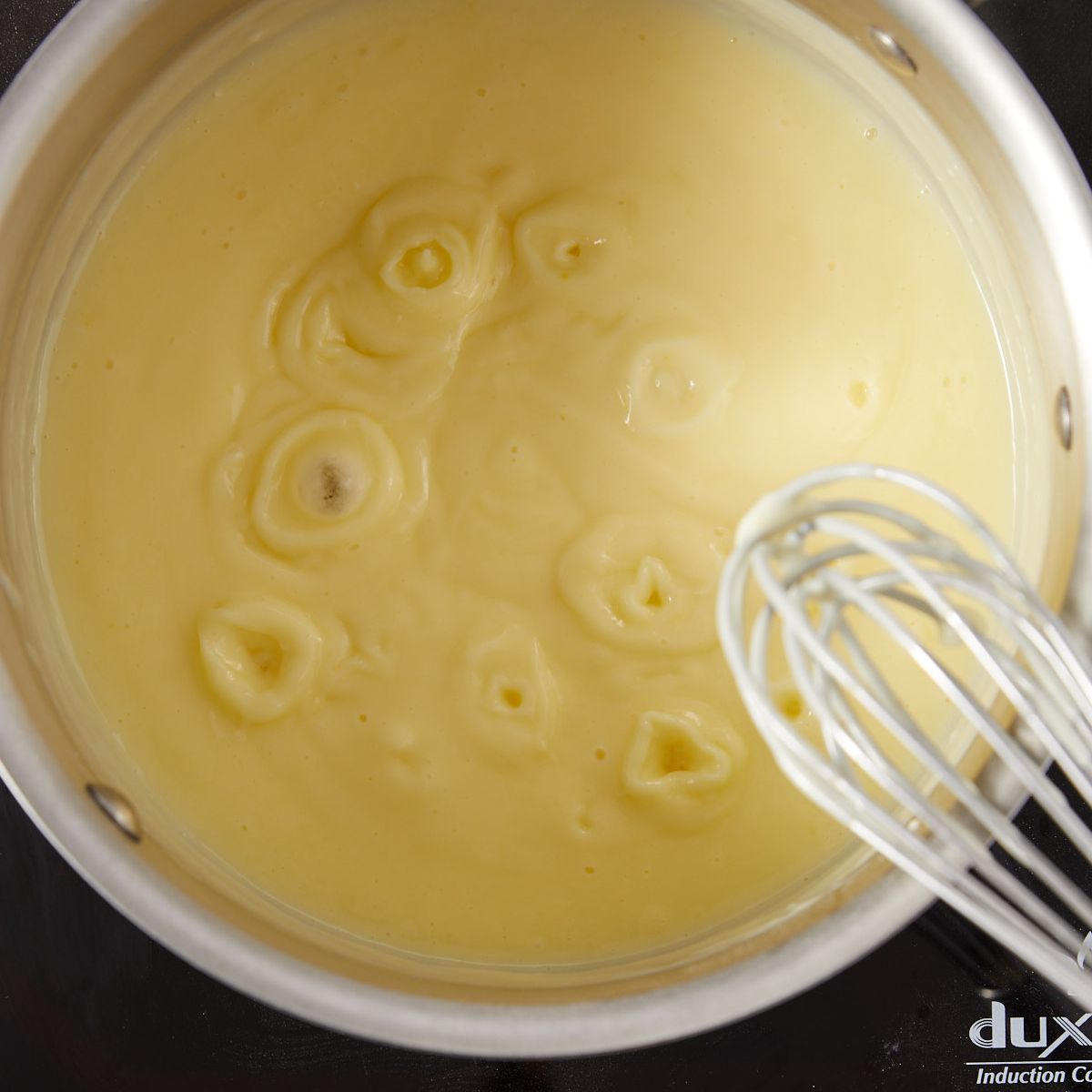Vanilla pudding cooking and bubbling in a saucepan on the stove.